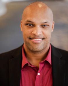 Photo of Dr. L. J. Randolph Jr. He is smiling and wearing a red button up with a black blazer.
